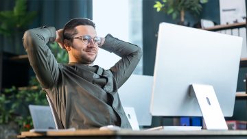 Immobilienmakler vor PC lehnt sich entspannt zurck